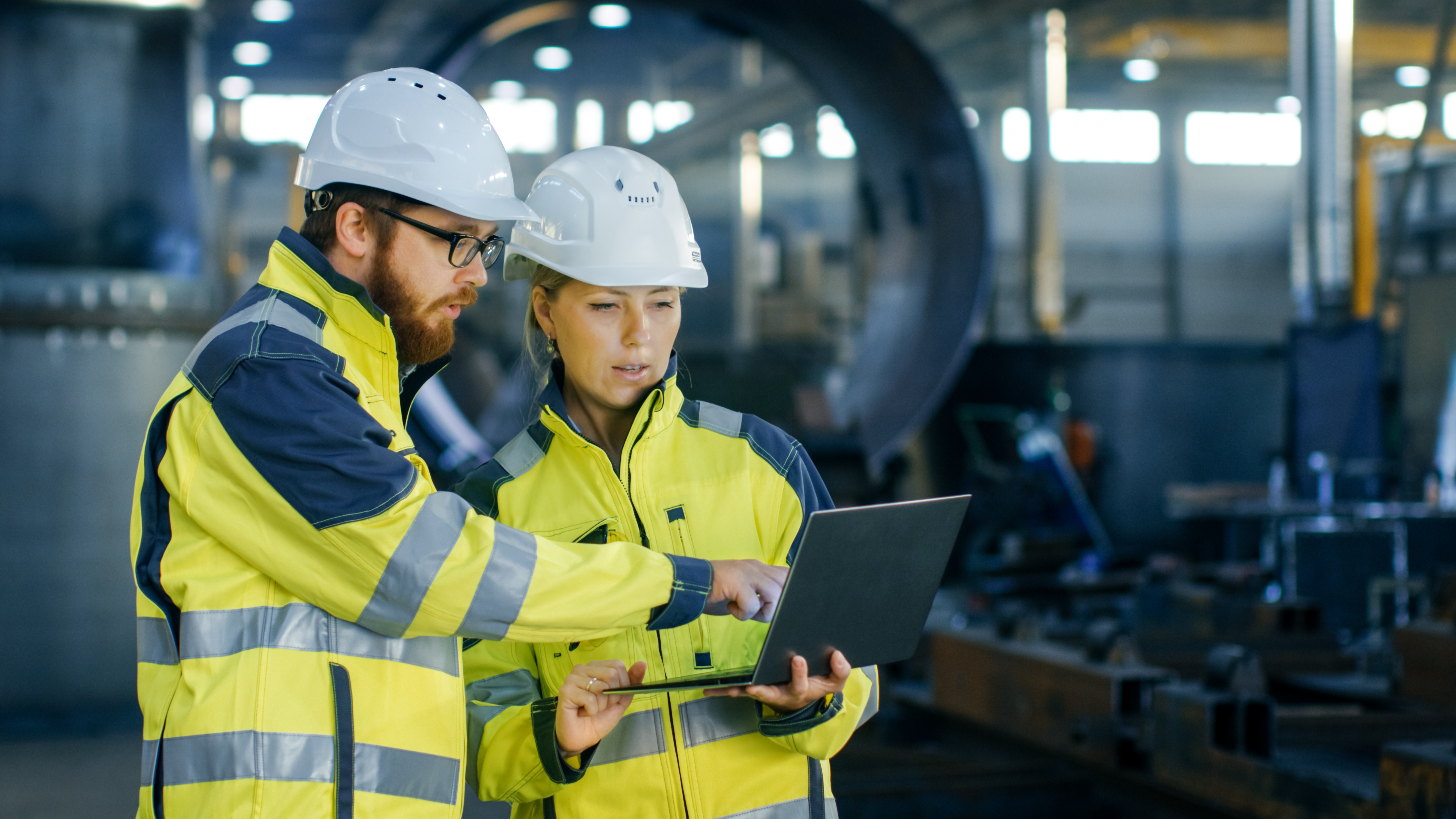 Kiwa inspectors wearing hard hats and high-visibility jackets reviewing plans on a laptop in an industrial setting