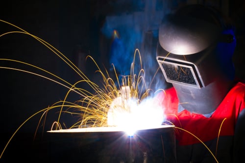 Svetsare i skyddsutrustning arbetar med en ljusstark svetslåga, omgiven av gnistor. Svetsare kan bli kvalificera sig för WPS och WPQR.