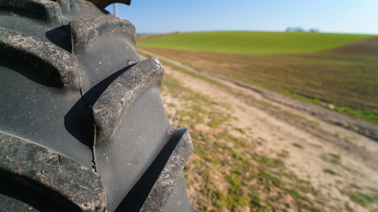 Närbild av ett traktordäck i förgrunden med ett landskap av åkermark och gröna fält i bakgrunden under en klarblå himmel.