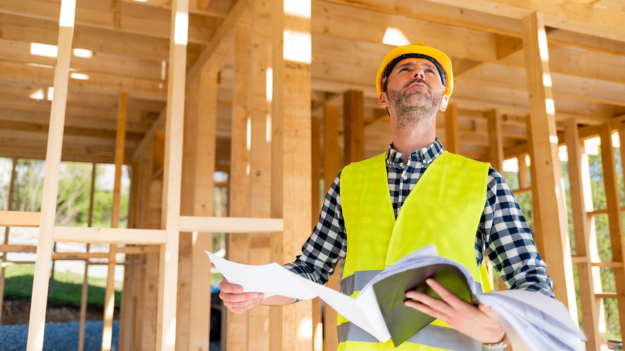 Manlig byggprojektledare med varselväst och bygghjälm på en byggarbetsplats.