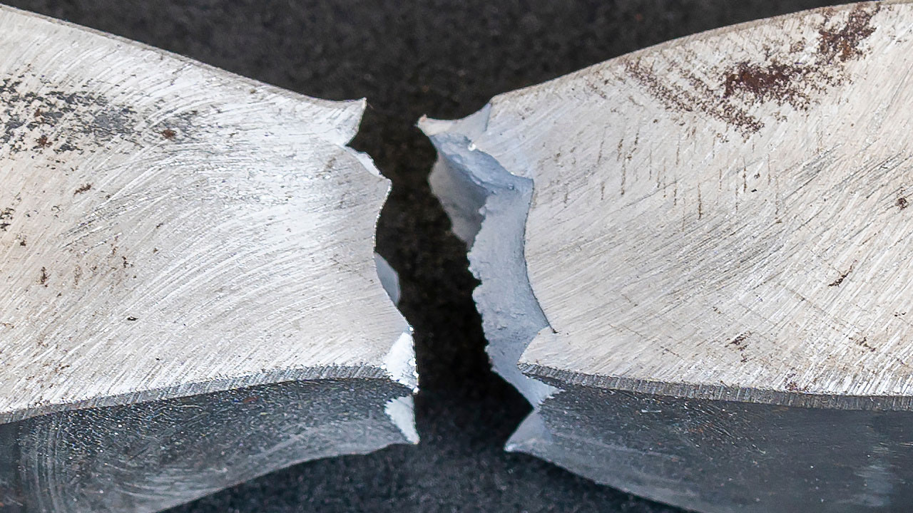 Hållbarhetstest för metall, förstörande provning. Brottyta av metall, med tydliga sprickor och ojämna ytor, fotograferad mot en mörk bakgrund.