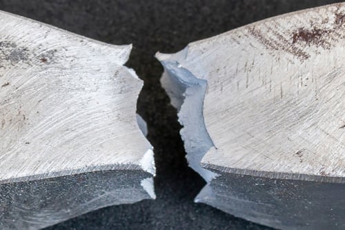 Hållbarhetstest för metall, förstörande provning. Brottyta av metall, med tydliga sprickor och ojämna ytor, fotograferad mot en mörk bakgrund.