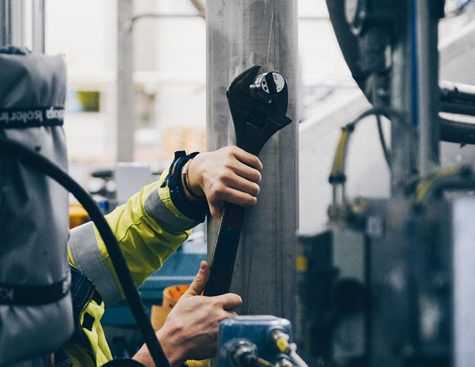 Person använder stor skiftnyckel för att justera maskin. 
