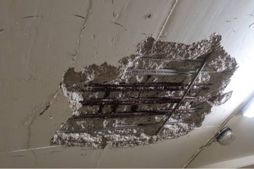 Betongtak med ett skadat område där armeringsjärn är synliga, omringat av sprucken betong.