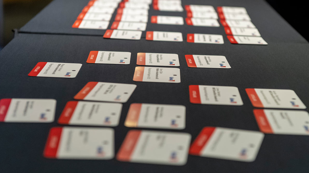 Namnskyltar med röda och vita etiketter utspridda på ett mörkt bord.