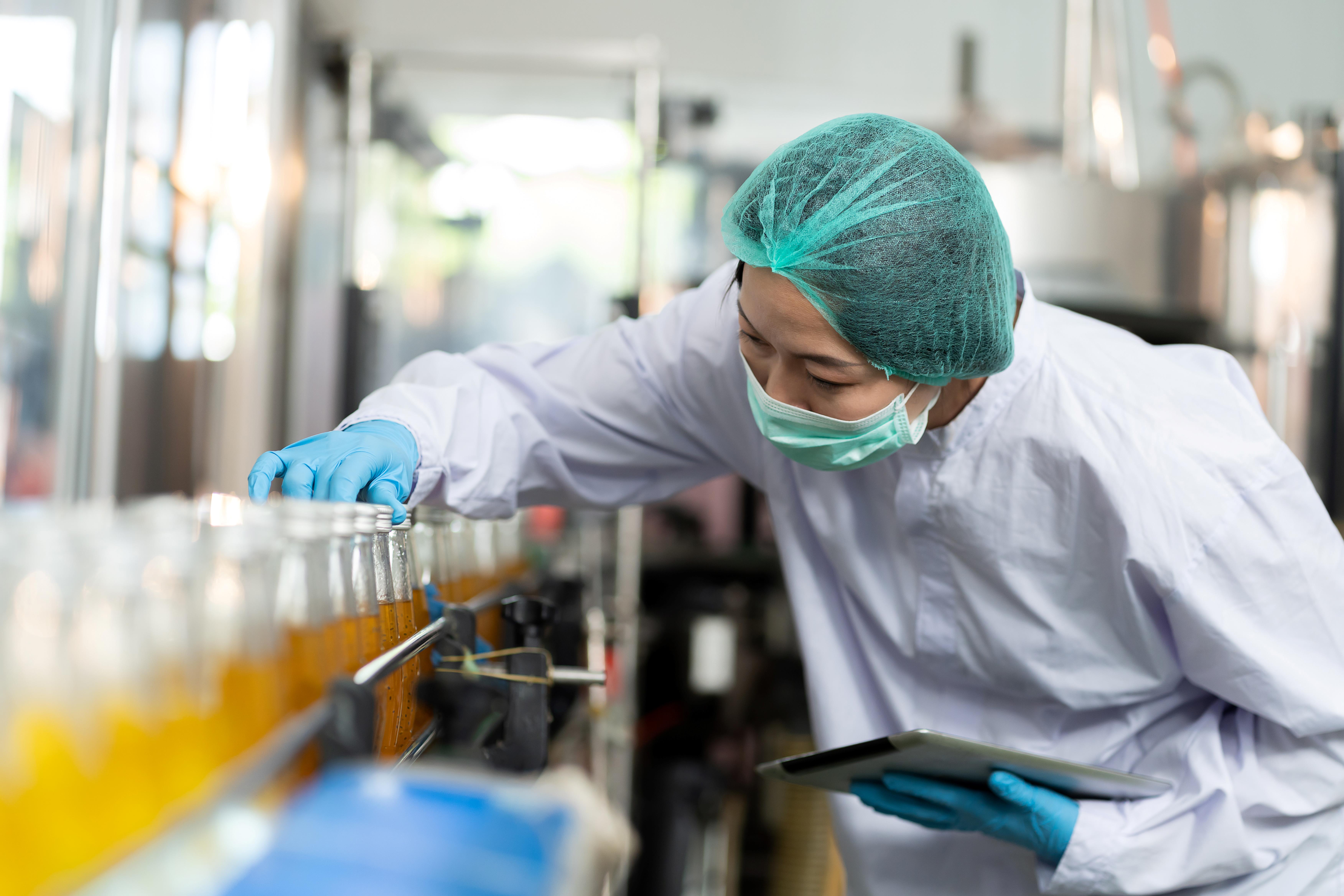 A Kiwa inspector wearing protective gear inspects glass bottles in a beverage production line