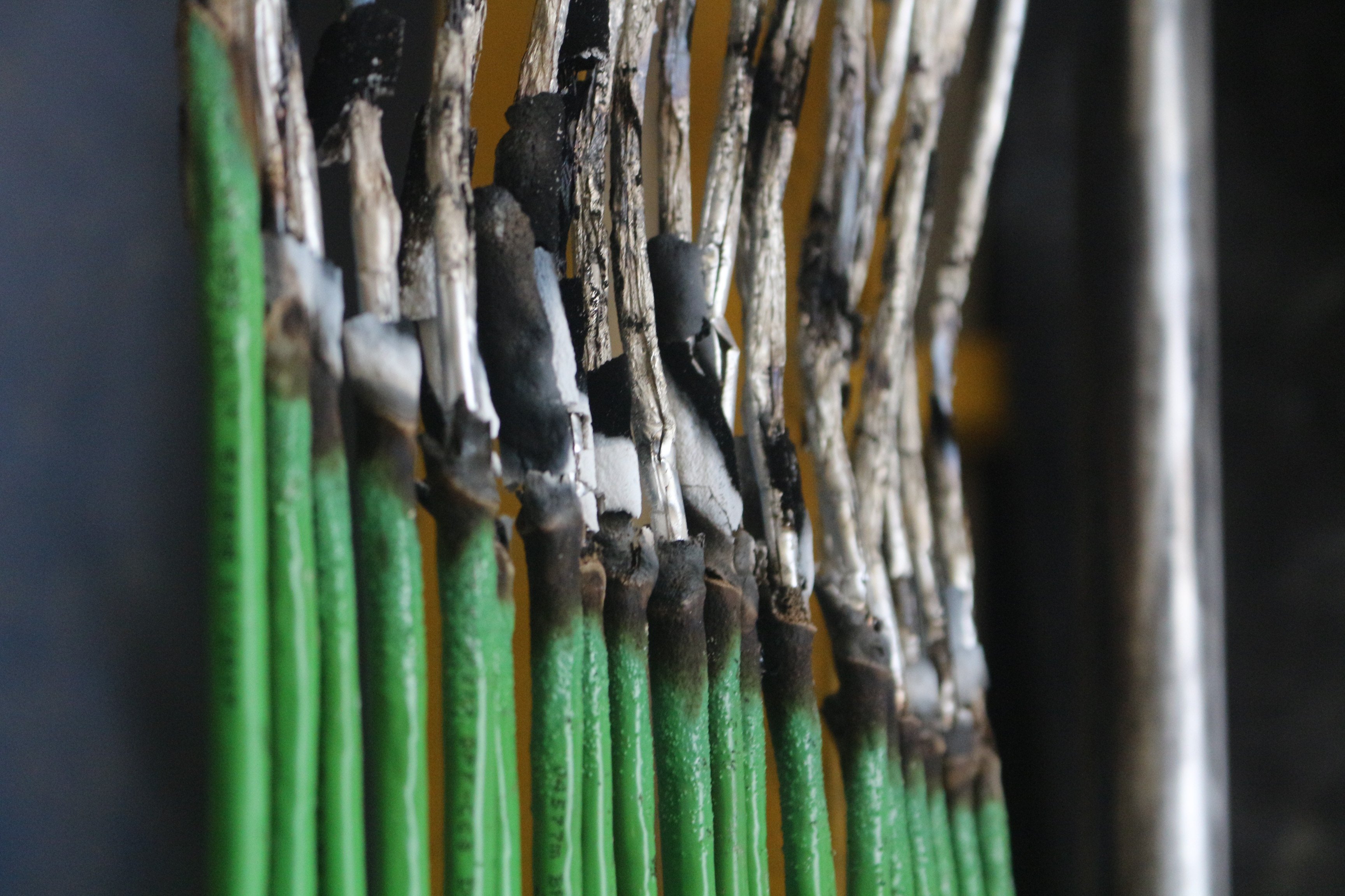 Close-up of multiple green wires with visible burn marks and damage, highlighting electrical safety risks