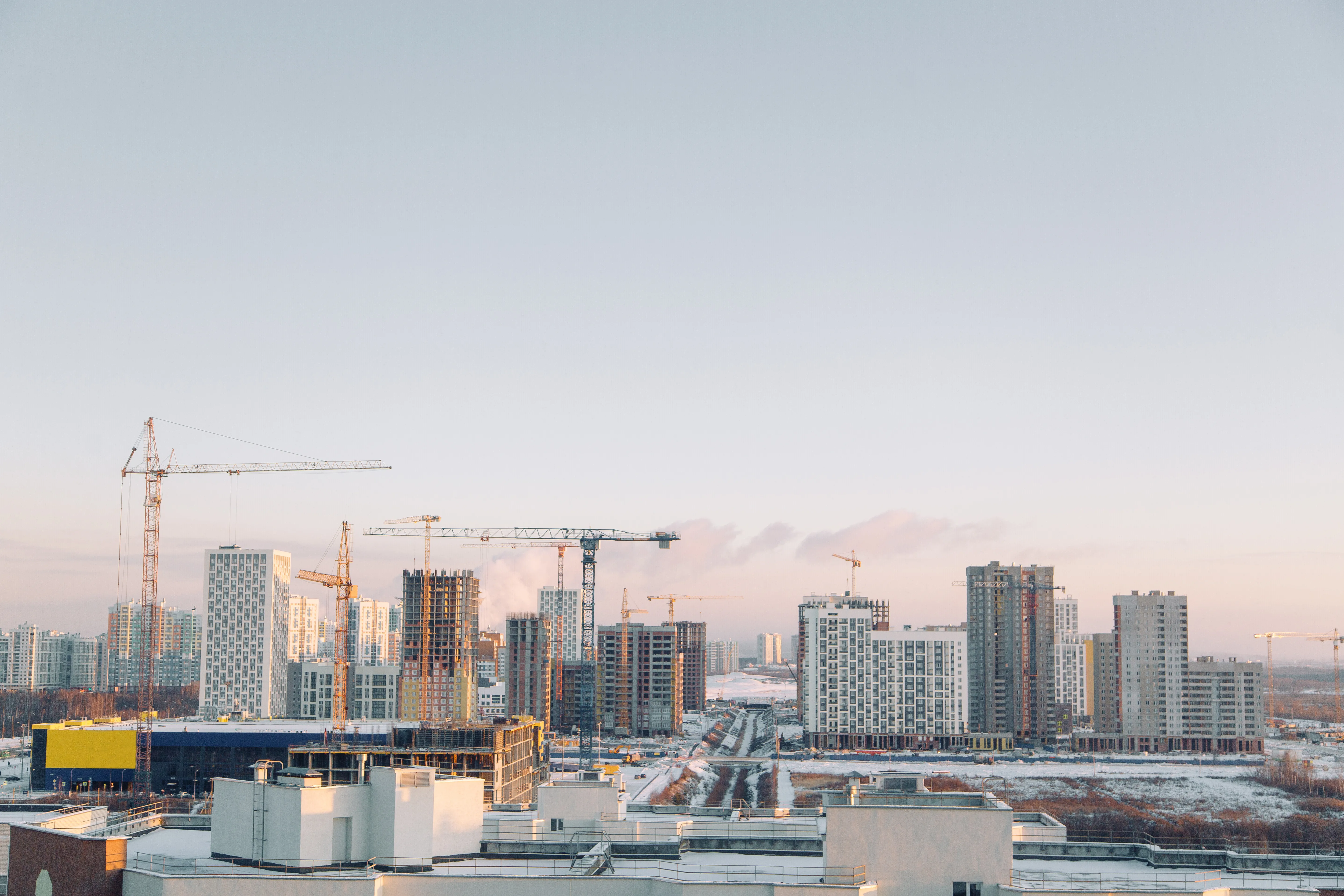 Urban skyline with high-rise apartment buildings under construction and multiple cranes at sunrise.