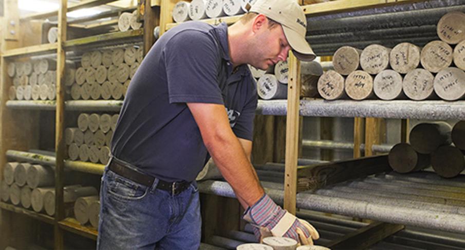 Kiwa employee examining geological core samples in a storage facility wearing casual attire and protective gloves