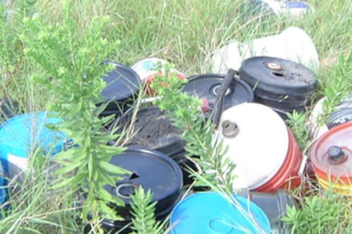 Plastic containers and canisters discarded in a grassy field, highlighting environmental waste and pollution