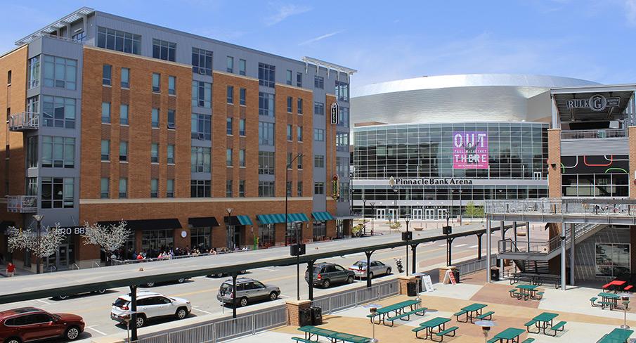 Downtown view of Lincoln, Nebraska featuring Pinnacle Bank Arena, street cafes, and parked vehicles in sunny weather