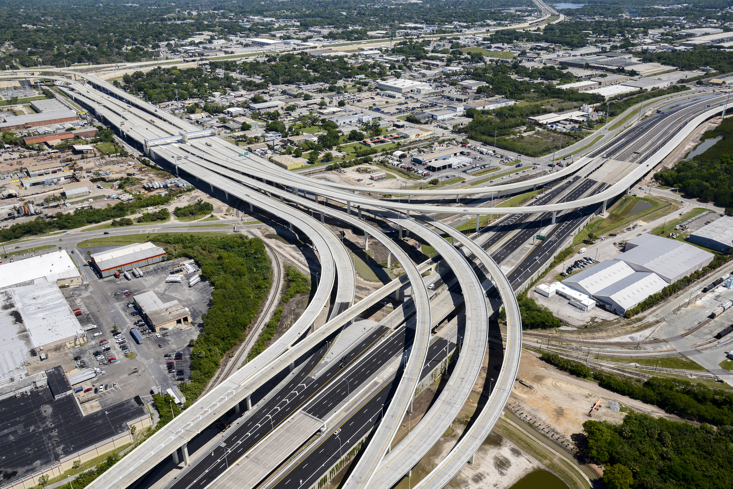 Aerial view of a busy highway interchange with multiple lanes and vehicles in motion, surrounded by green spaces, showcasing transportation infrastructure.